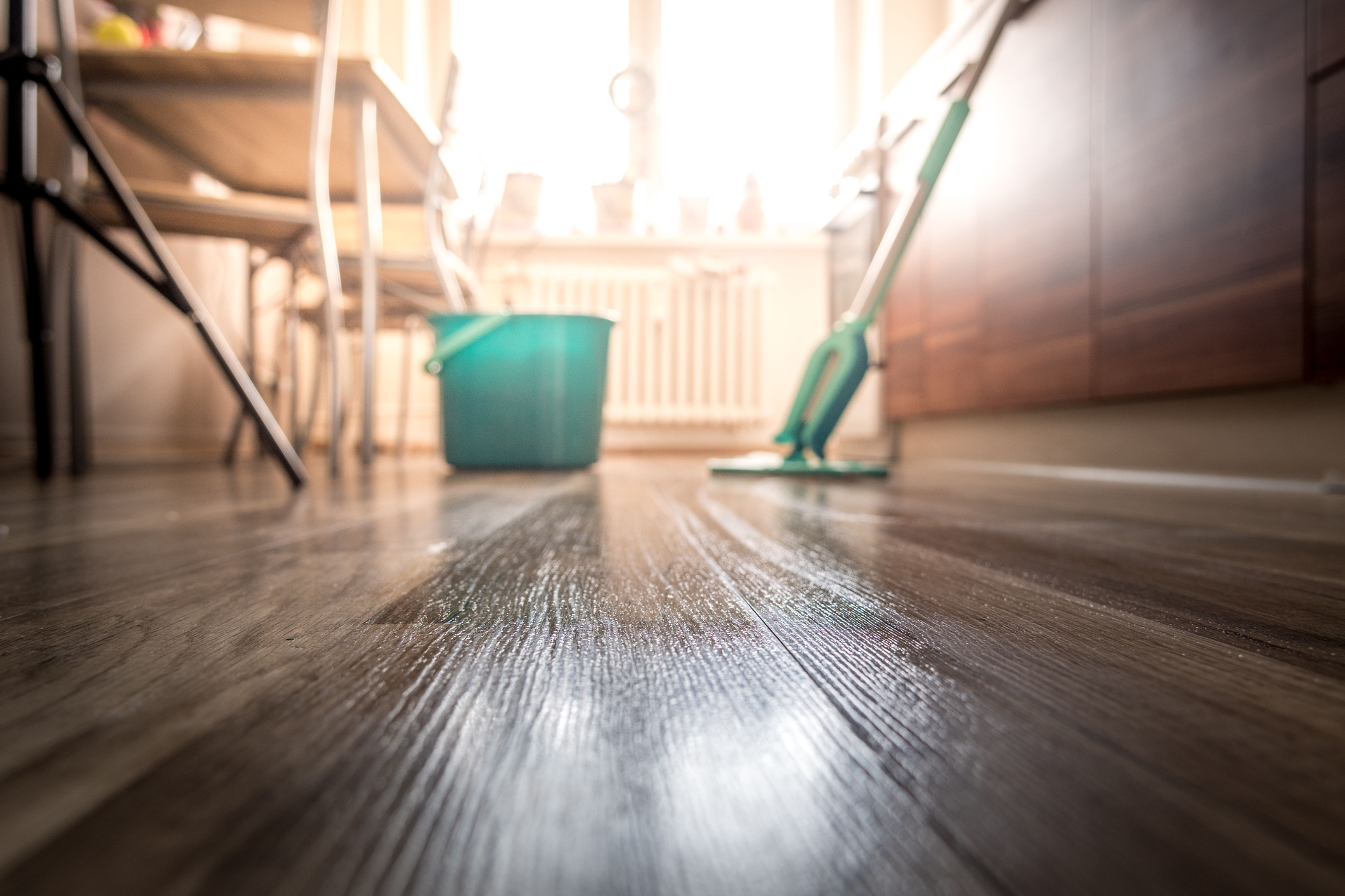 A clean wood floor with a mop and bucket of soap in the background