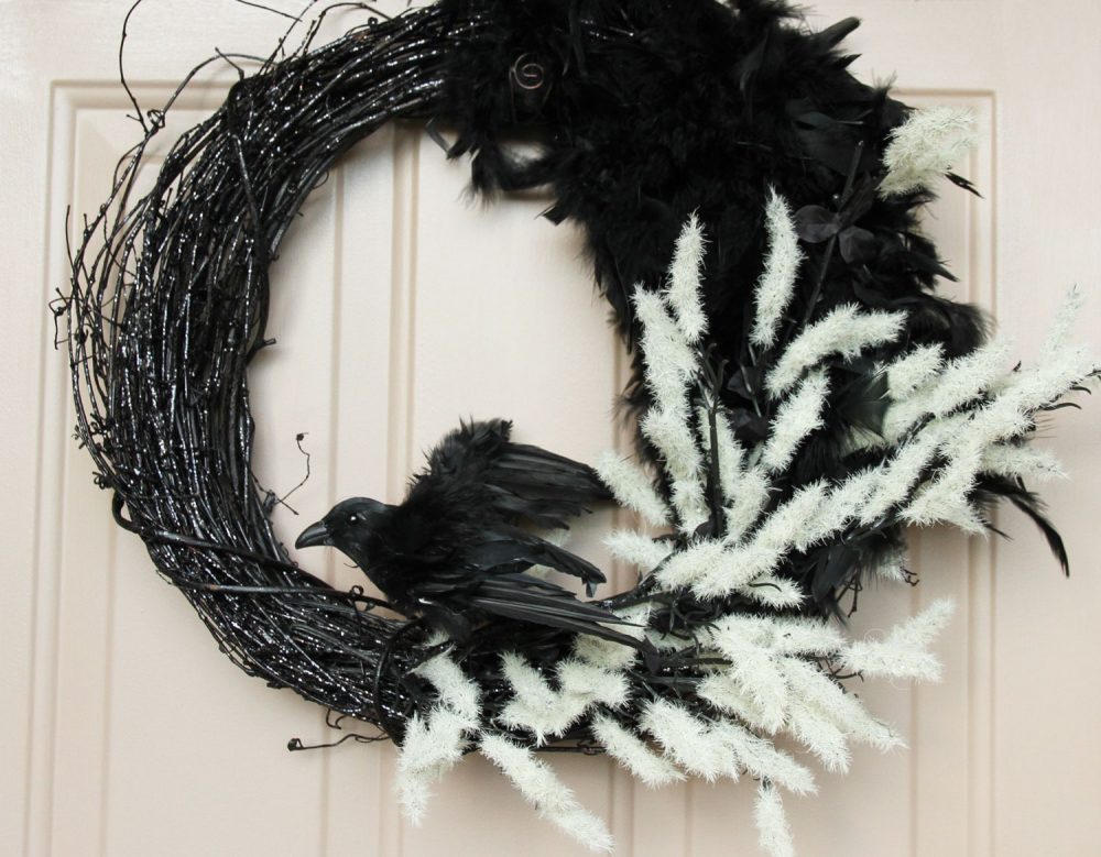 Black wreath hanging on front door with black crow and black and white feathers