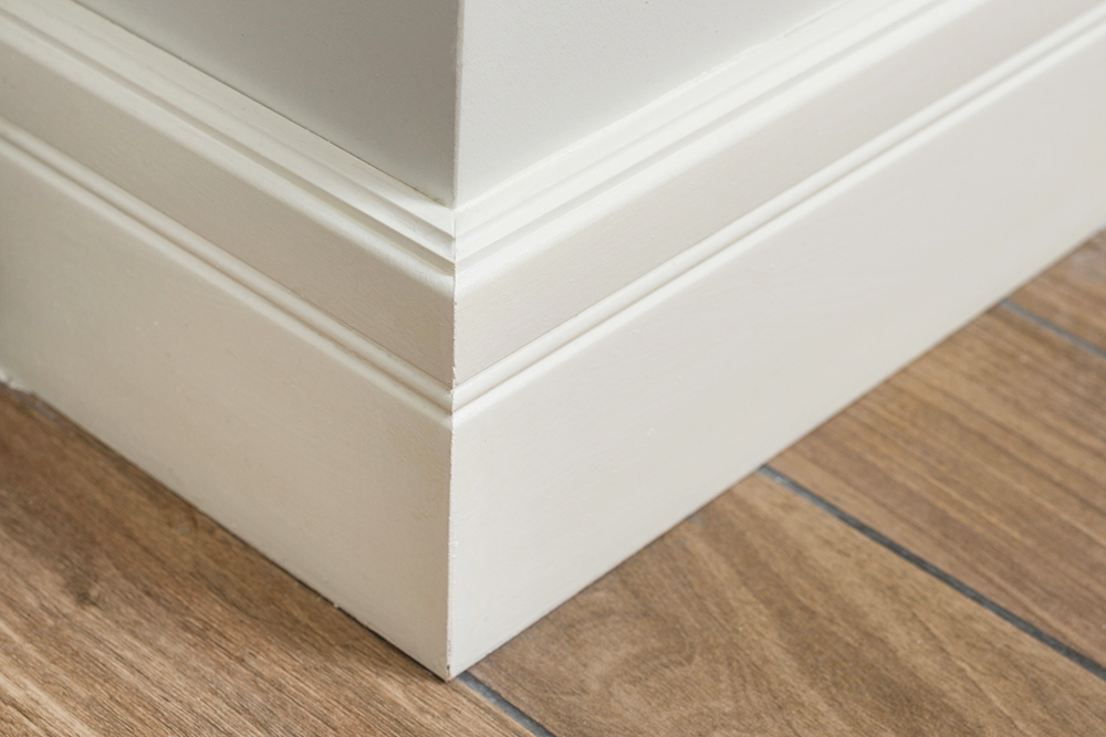A closeup of a white corner baseboard against a hardwood floor