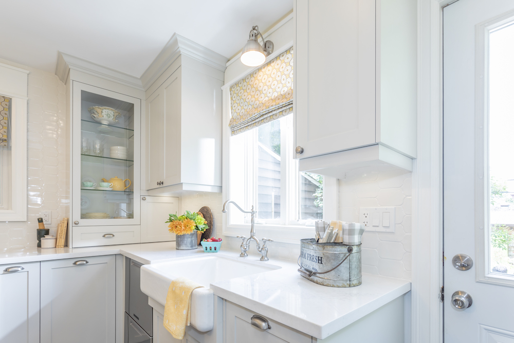 A crisp white kitchen renovation with glass cabinets, farmhouse sink and traditional crown mouldings at the top of the cabinetry