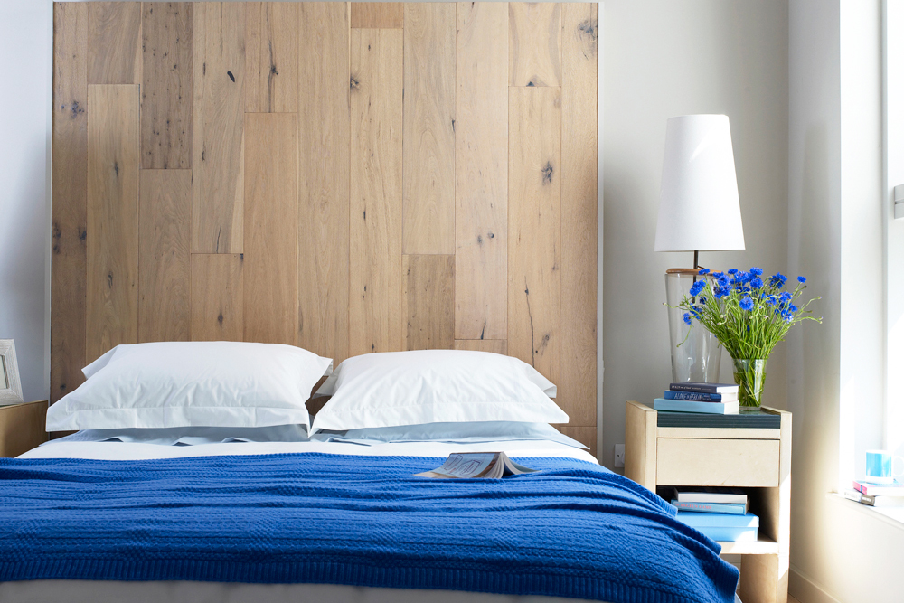 A double bed with a blue blanket against a tall wood headboard