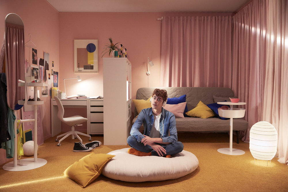 A teen hanging out in his dorm room on a floor pillow while listening to music
