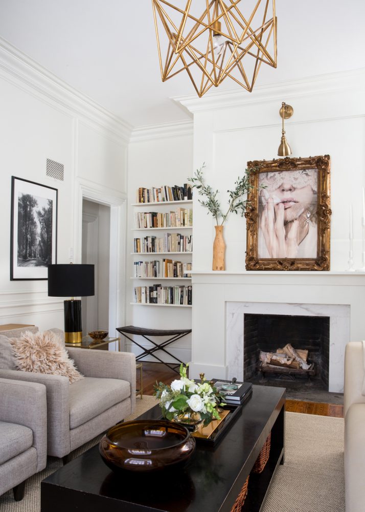 Neutral living room with white walls and light beige furniture. Above the white fireplace is a portrait in a gold statement frame.