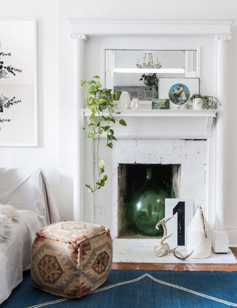 A white fireplace with a blue rug in front. Inside the fireplace is a large dark green vase.