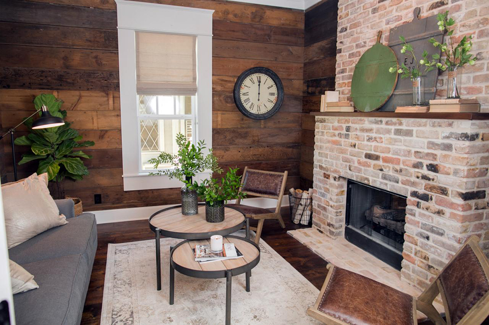 Warm, rustic living room with shiplap walls and brick fireplace stacked with firewood.