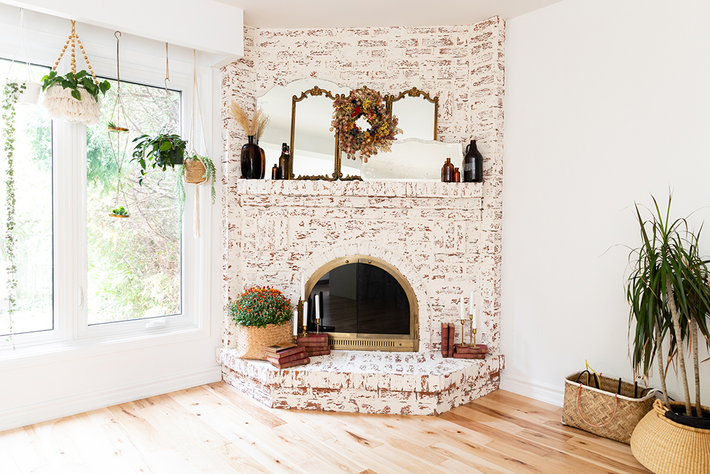 Bright living room with a brick fireplace smeared white. Around the fireplace are a number of plants in various sizes