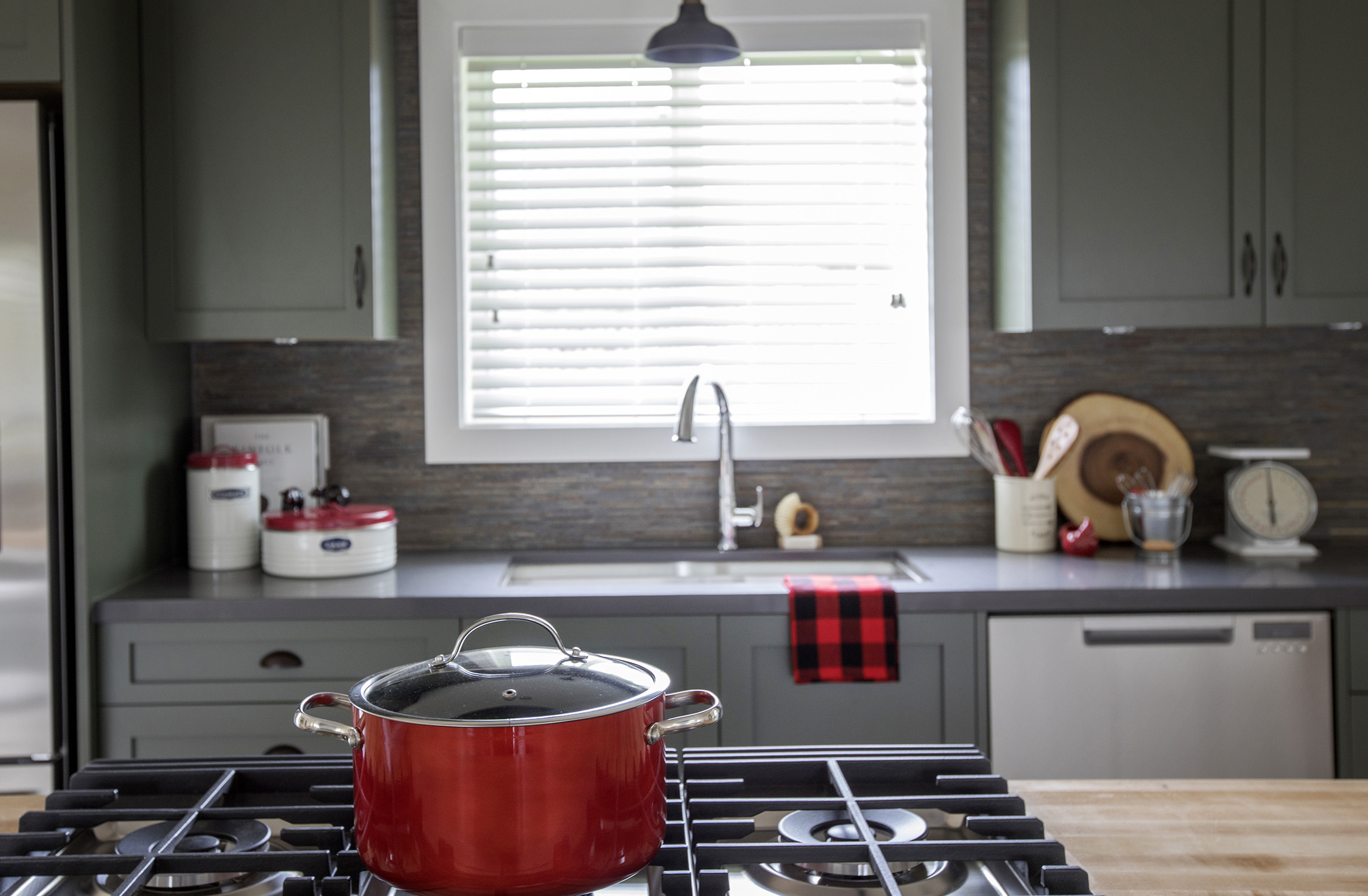 Making use of the complementary colour wheel, ruby-red kitchen accessories are set off against the sage-green cabinetry.