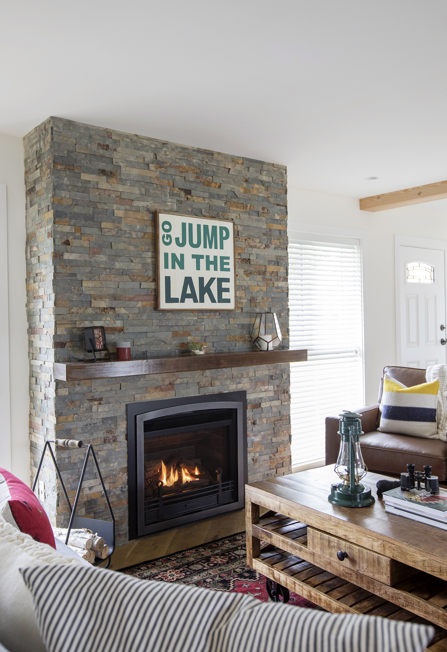 A jump in the lake sign sitting above a stone fireplace.