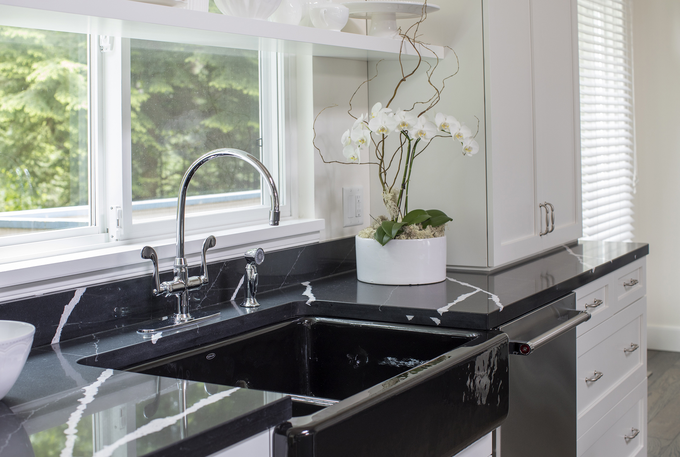 The back wall of the kitchen features a shiny, black apron sink and black quartz countertops with white marble graining.