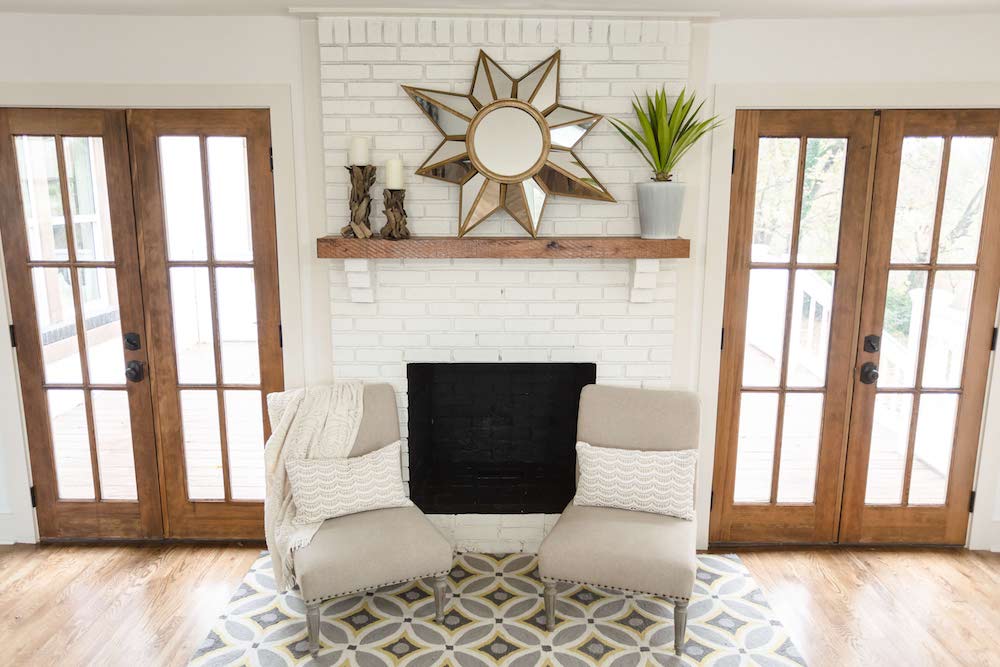 Farmhouse living room with French doors and white-painted brick fireplace surround.