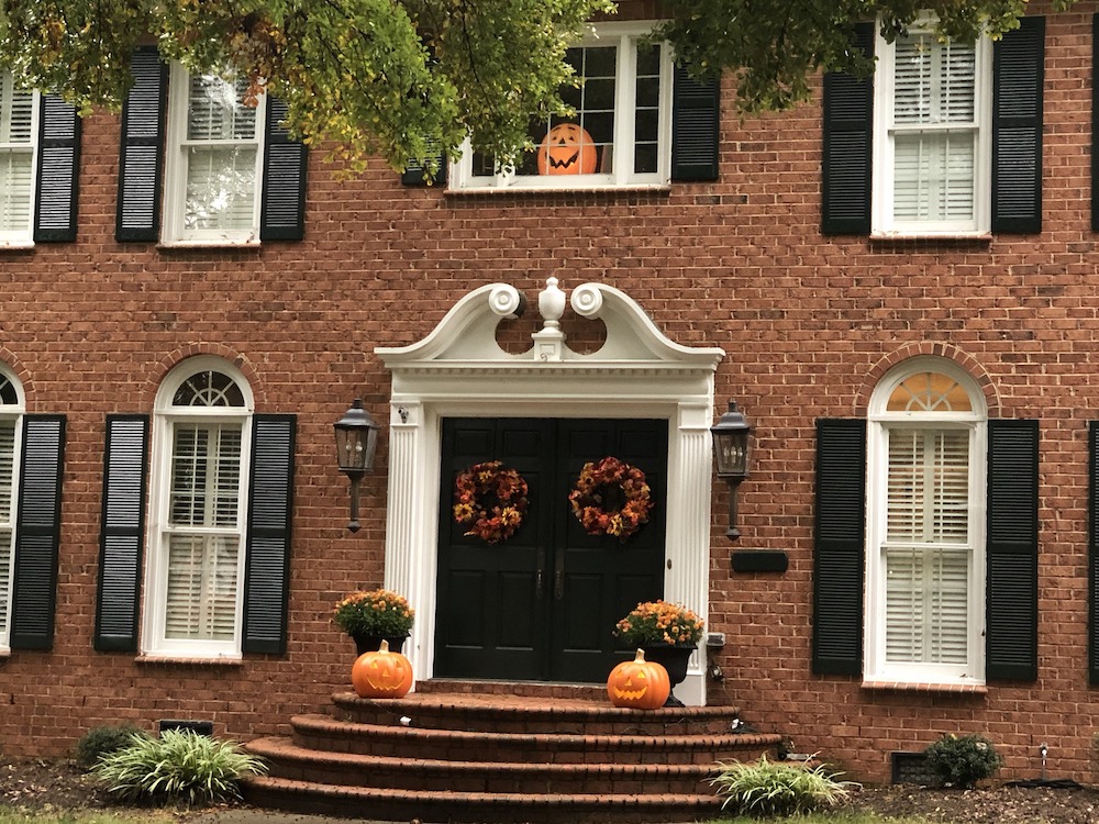 front of house with two pumpkins and two pots of mums on front porch