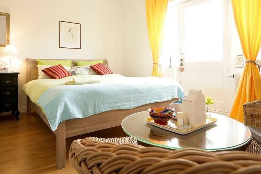 Brightly-lit bedroom with plenty of natural sunlight and wicker furniture surrounding the double bed
