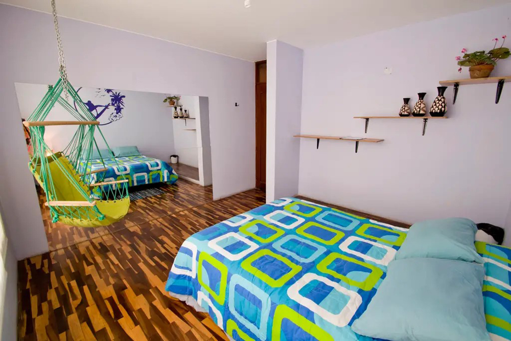 Spacious bedroom with patterned wood floors, bright double bed and chair swing