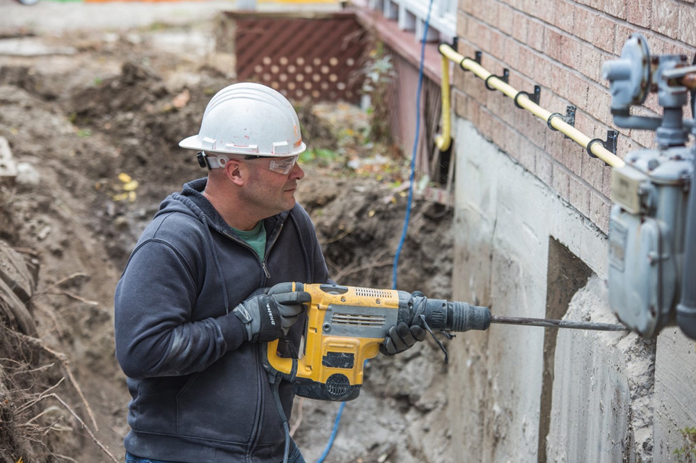 Bryan Baeumler wears a hard hat and works on the exterior of a renovated home