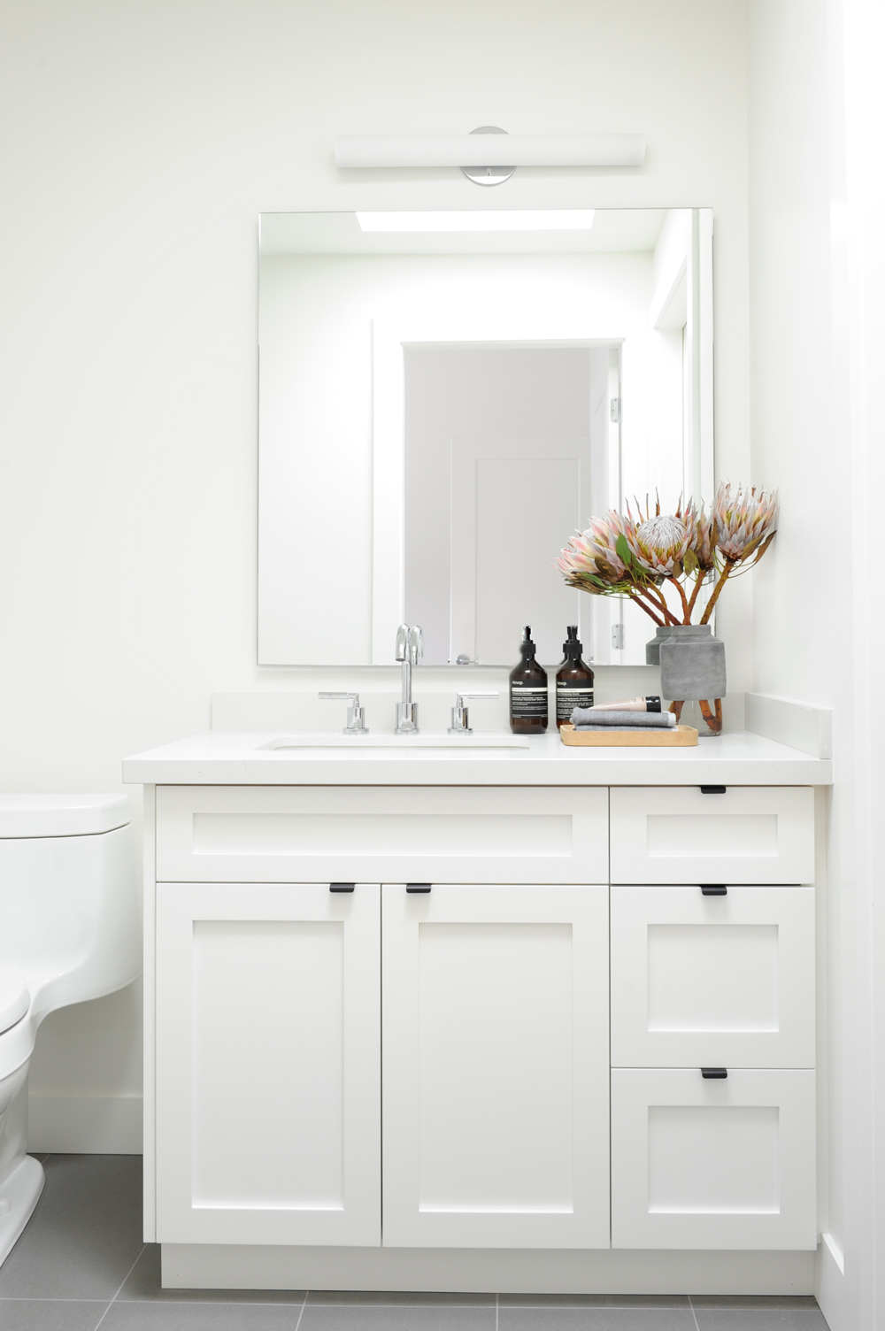 all white bathroom with square unframed mirror, two Aesop pump soaps, and Protea arrangement