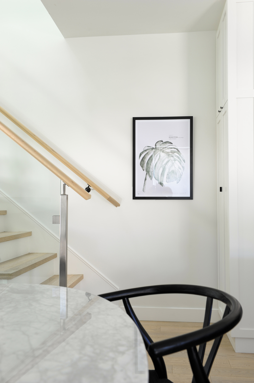 framed palm leaf at bottom of stairs, black chair and marble table top