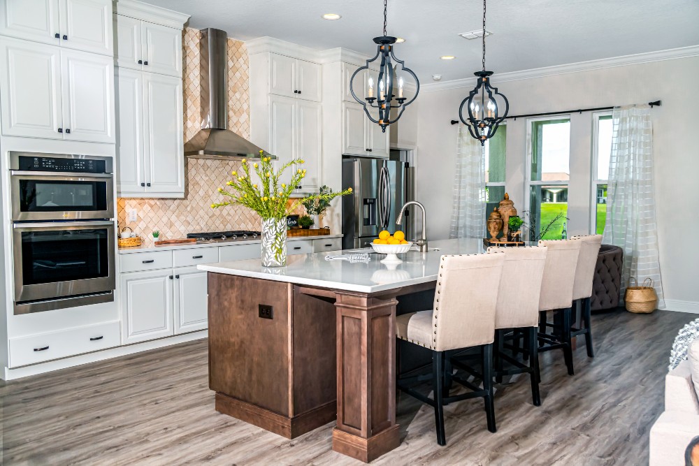 A kitchen with white cabinetry, stainless steel appliances, countertop range, white counters, and an island with sink, dark cabinetry, and upholstered stools.