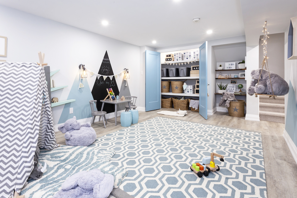 A pastel blue, white and grey basement playroom with large area rug and extensive storage space