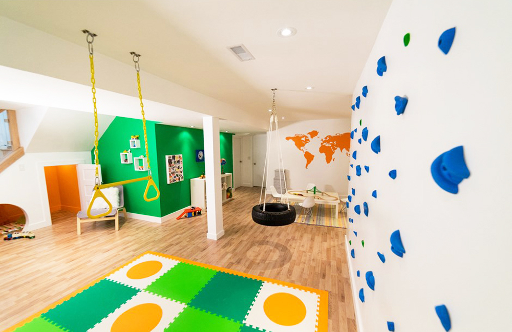 A vibrant yellow and green basement playroom with a mini rock climbing wall and tire swing