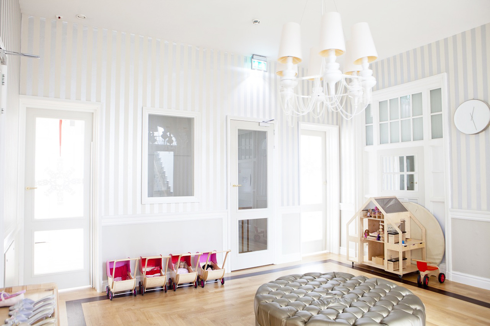 White and grey striped wallpaper in a playroom with a dollhouse and unique light fixtures