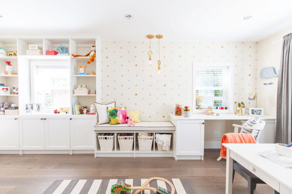 A spacious white playroom with polka dotted wallpaper, storage space and a little desk area for studying