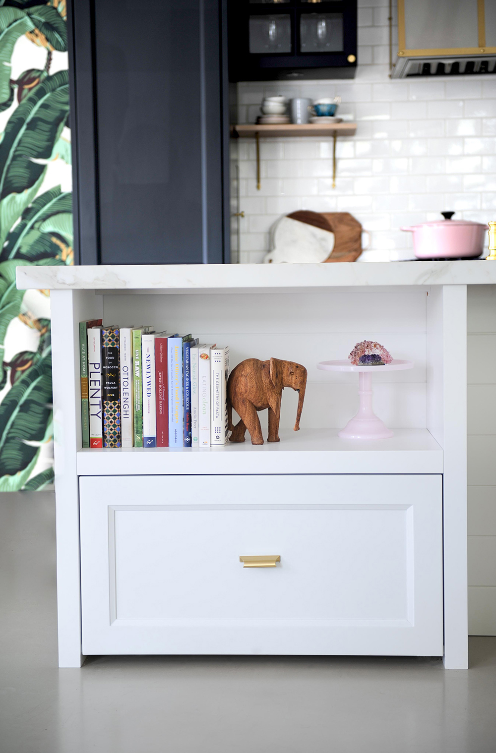 close up of kitchen island with open shelf with cookbooks, wooden elephant and pink cake stand