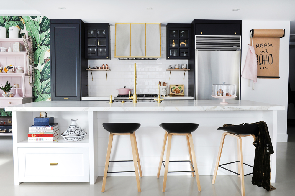 white kitchen with island, black cabinets, three black and wood stools with a coat on one
