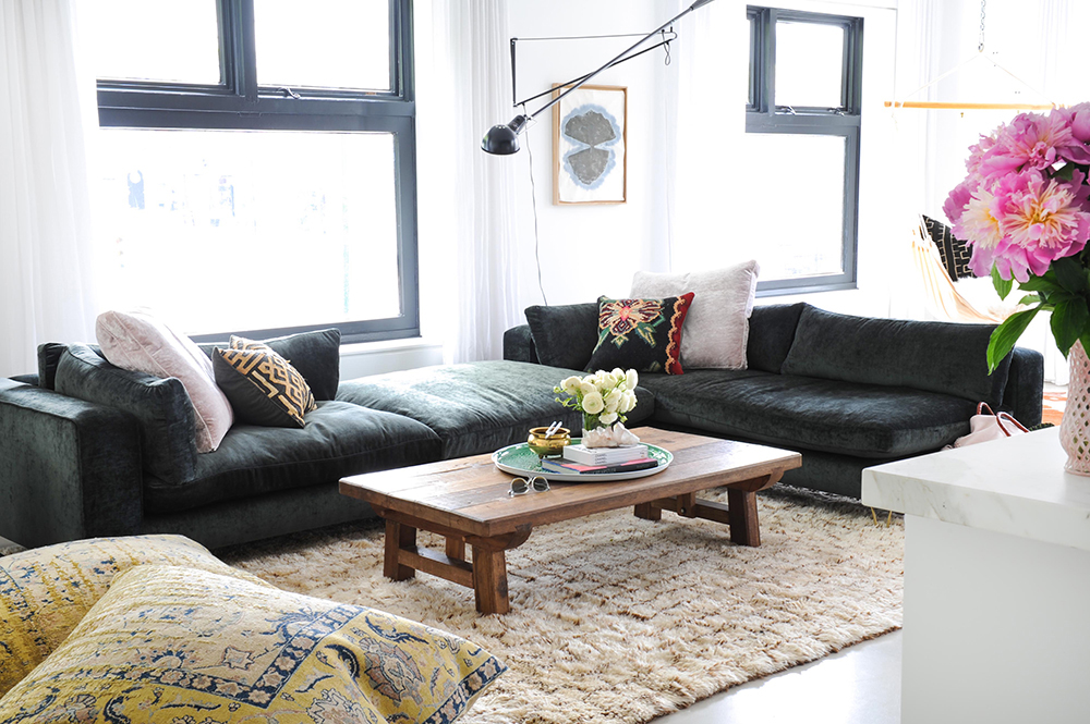 loft living room with floor cushions bottom left, pink flowers on right, dark sectional and low wood coffee table