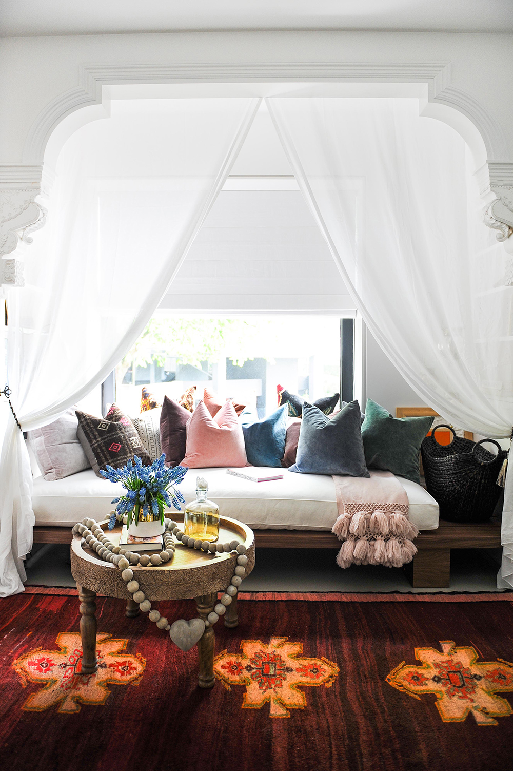 white curtained daybed covered in cushions in an alcove, colourful rug with three orange designs