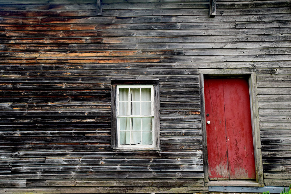 A wooden house with bright red front door in need of paint