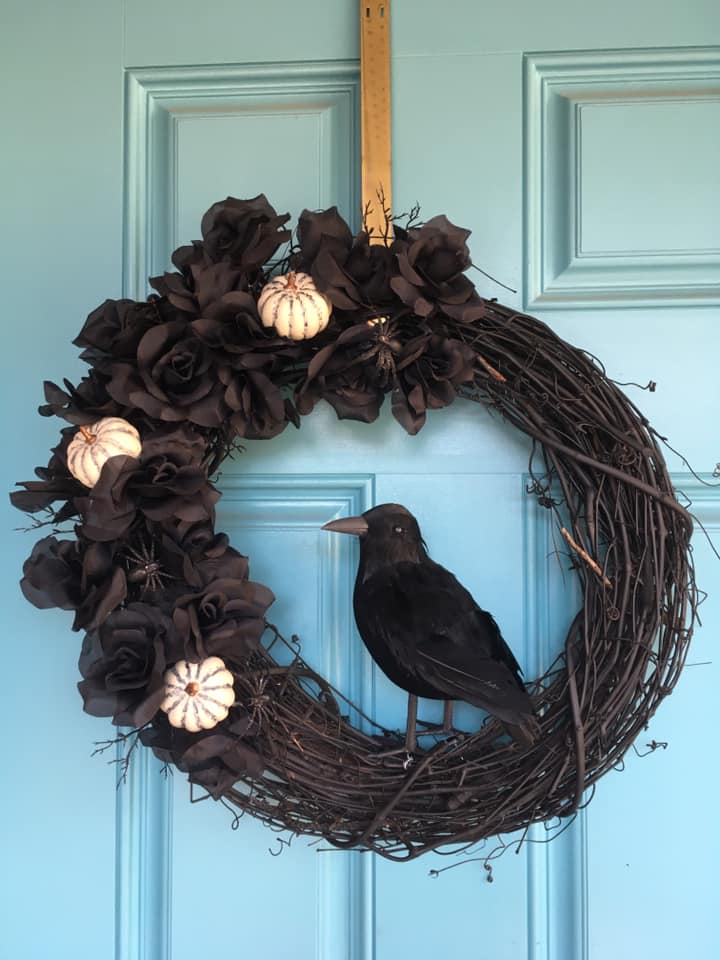 Black crow sitting on black Halloween wreath with little white pumpkins
