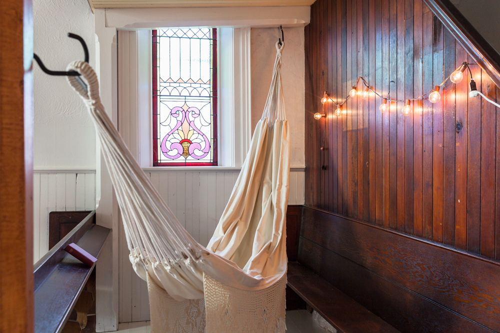 A thick white hammock hanging between two pews in a church renovated into a home
