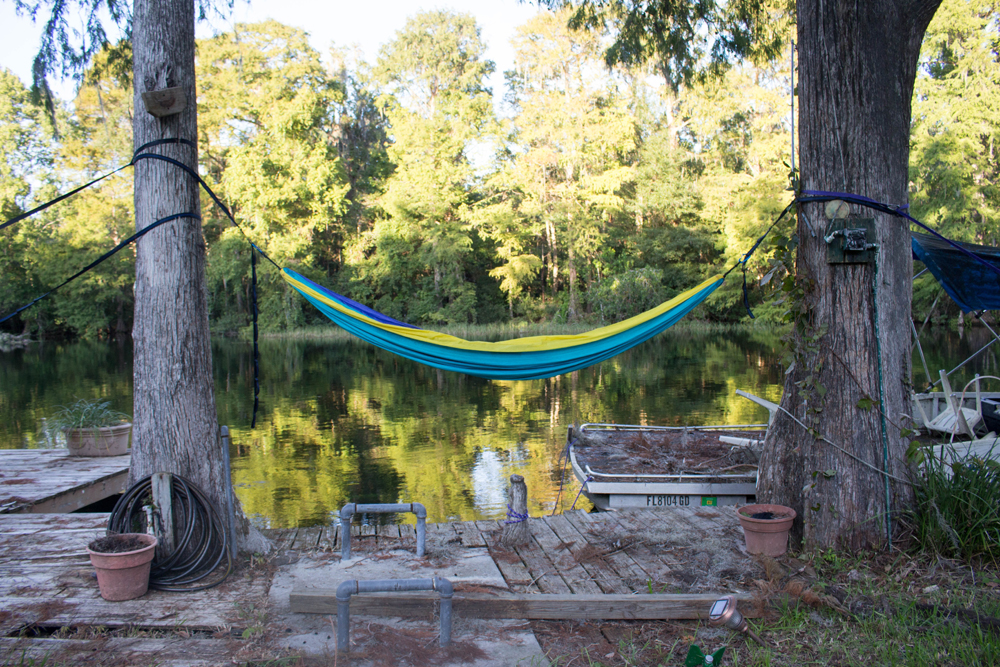 A brightly coloured hammock strung between two trees on a dock by the lake