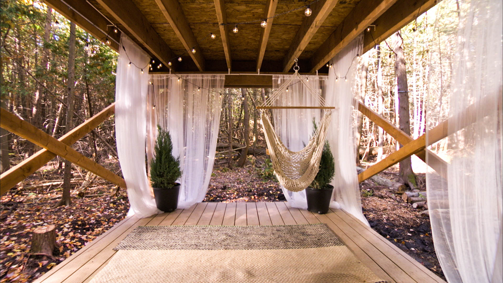 A backyard oasis with a simple hammock swing, transparent curtains and string lights
