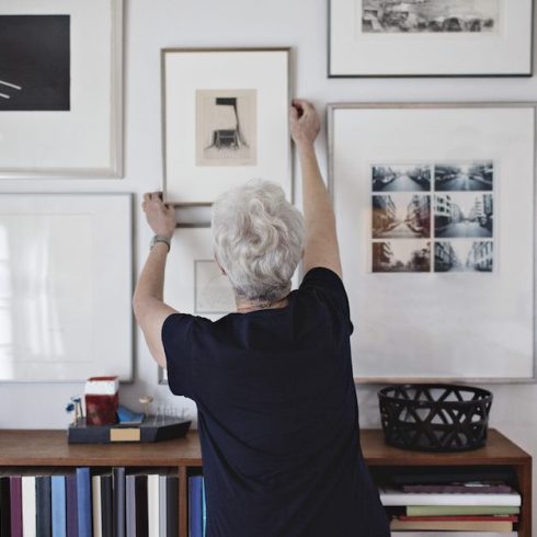 woman hanging pictures on wall over bookshelf at home