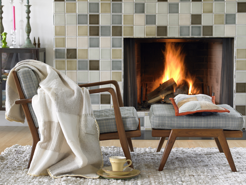grey armchair and footrest in front of tiled fireplace with pillow, blanket soft rug on the floor