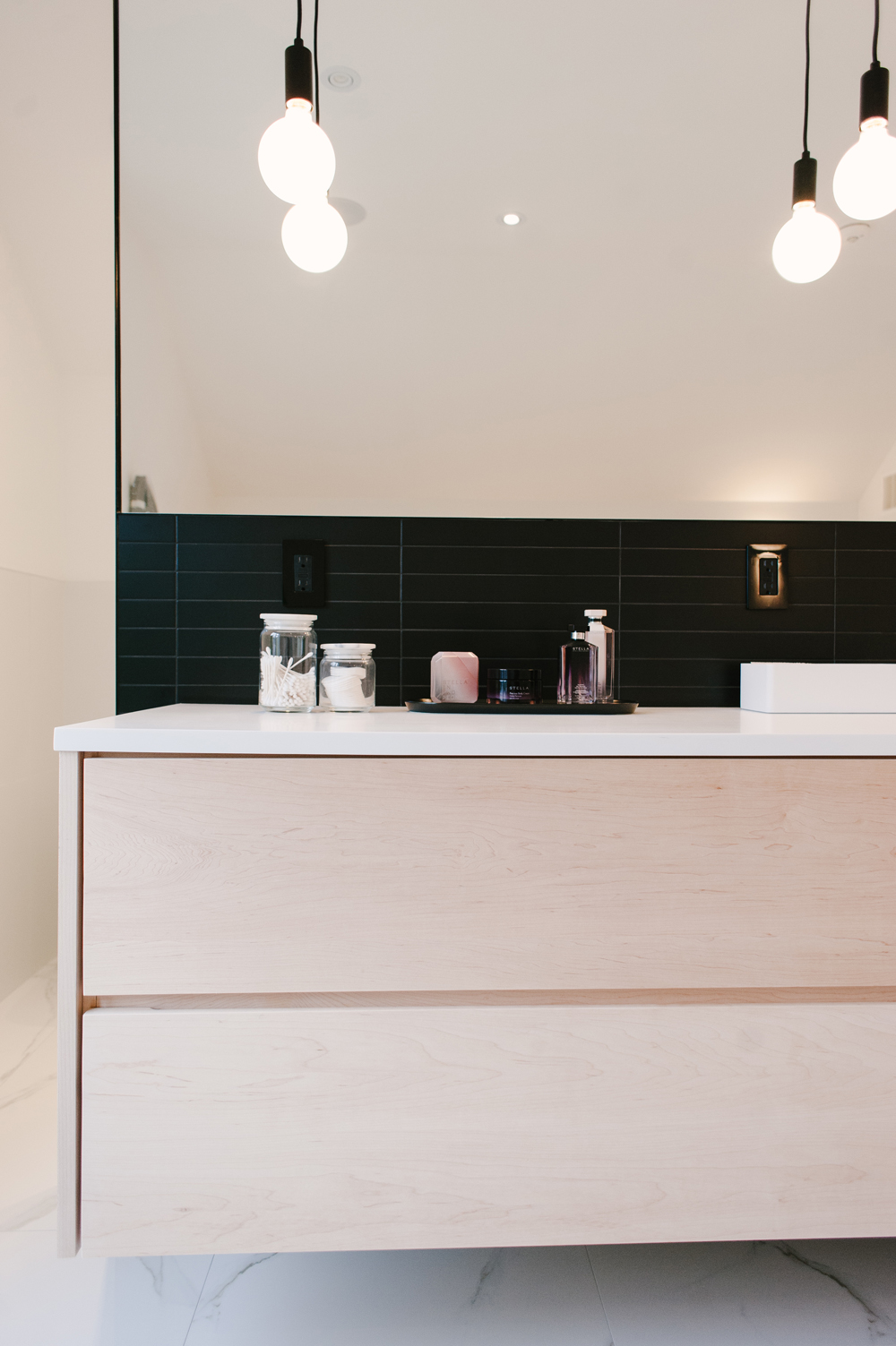 Floating wood vanity with black tile bathroom backsplash