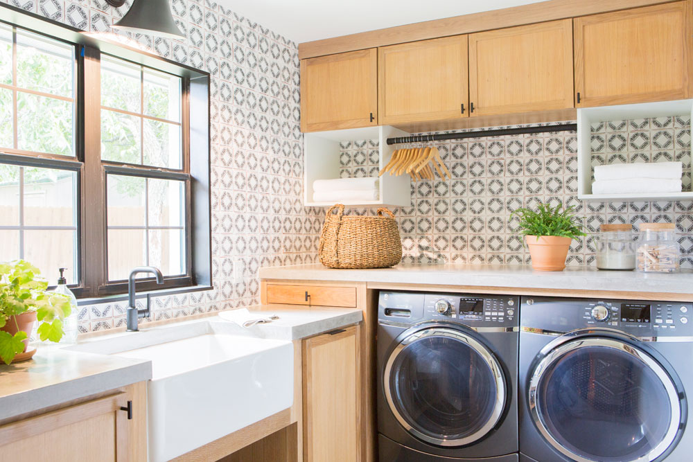 Modern farmhouse laundry room design with patterned backsplash and wooden cabinetry.