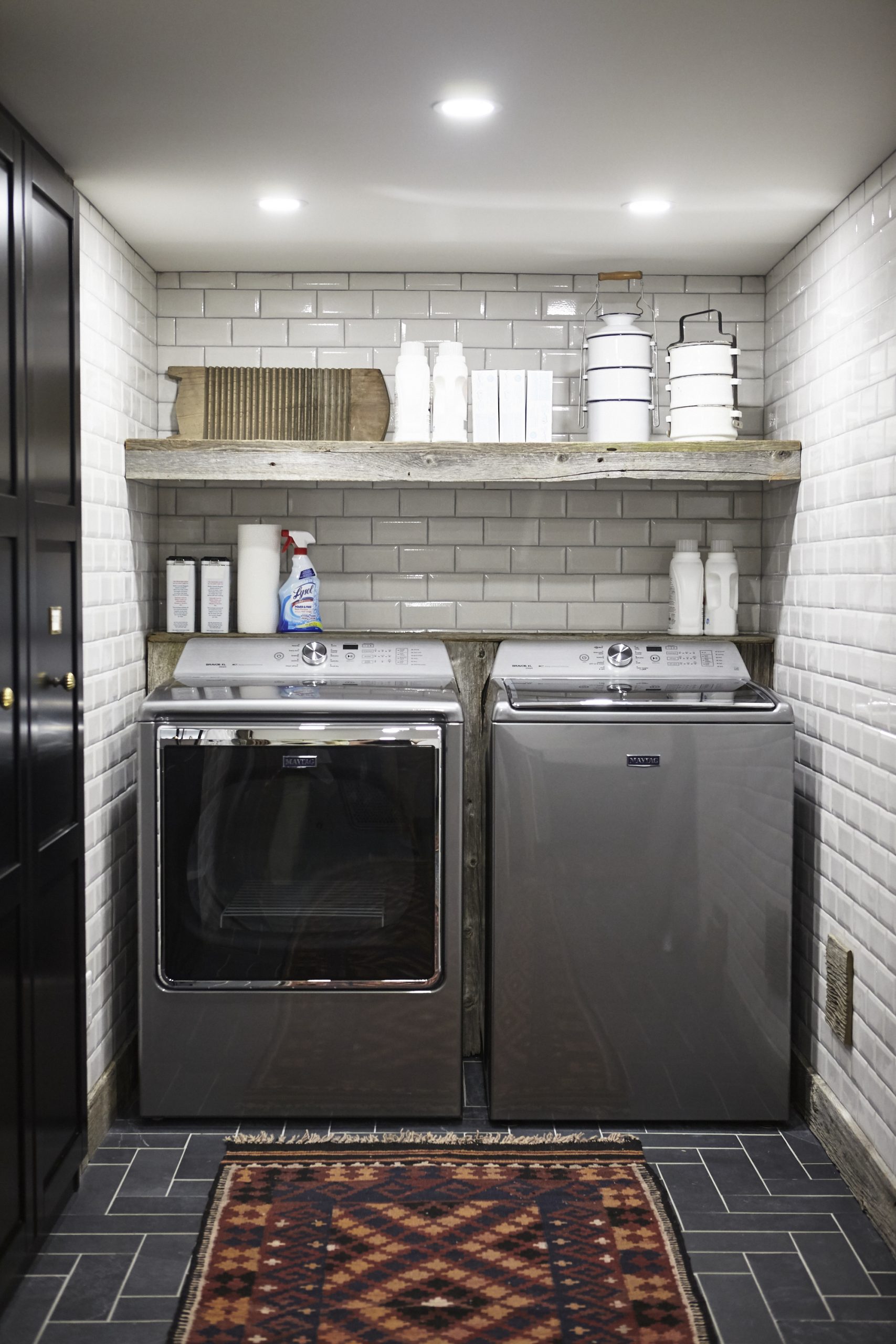 laundry room with floor-to-ceiling white subway tiles and wood open shelving.