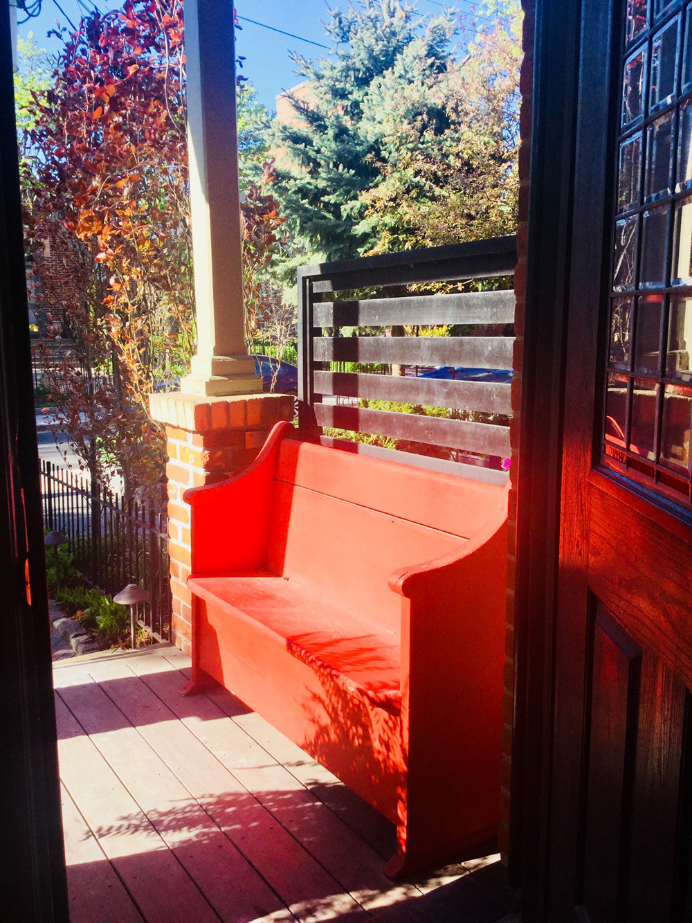 An old church pew on a tiny front porch painted a cheery bright orange-red