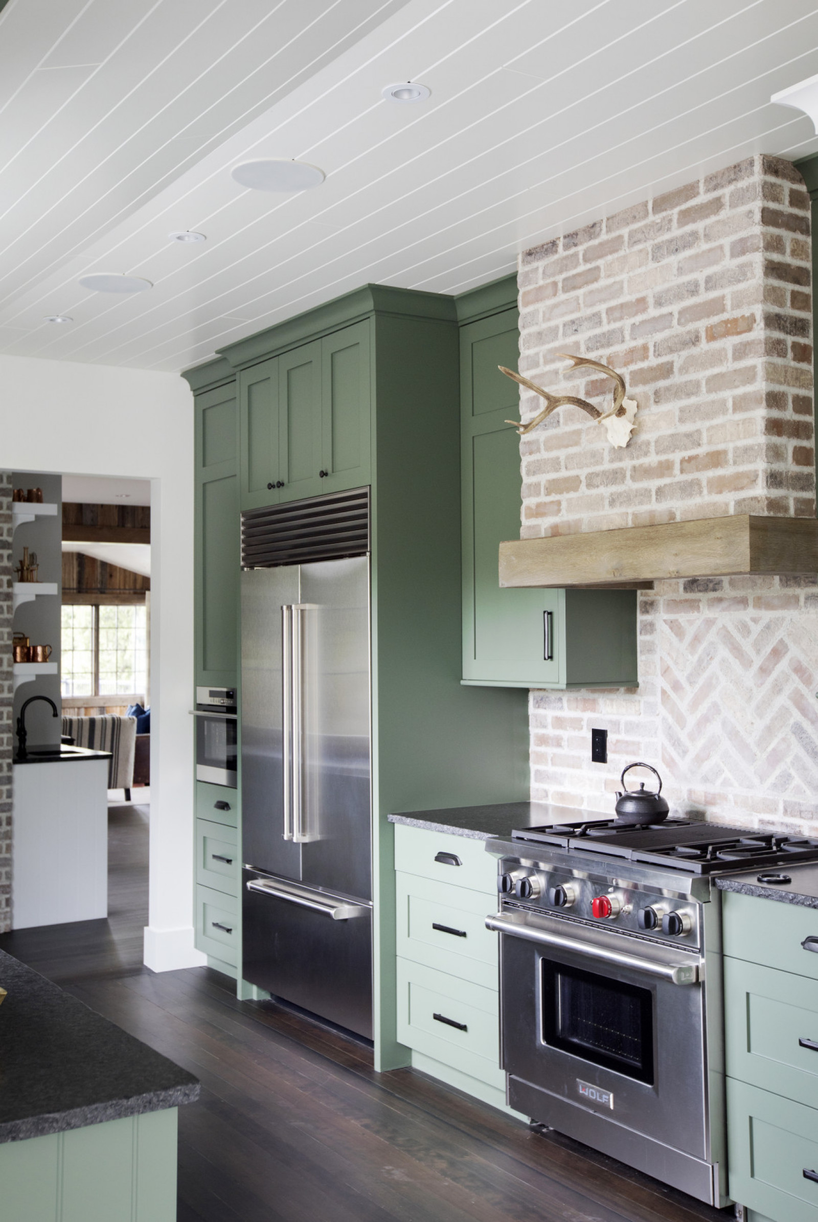 green cabinet kitchen with pale brick backsplash and animal skull over wolf range