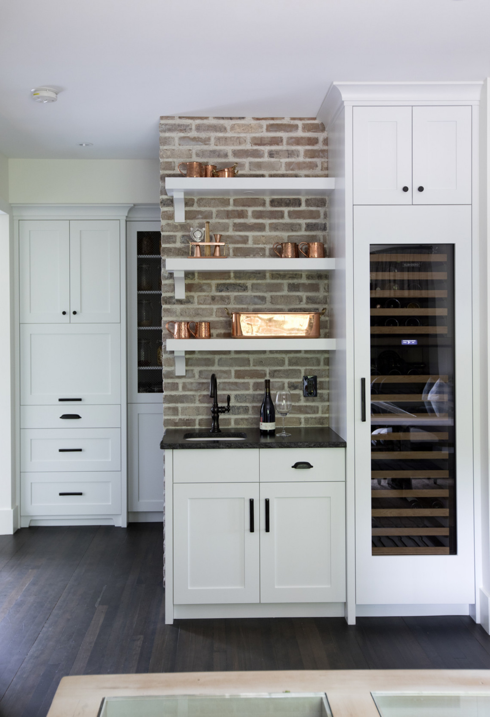 exposed brick wall with floating shelves beside wine fridge in kitchen