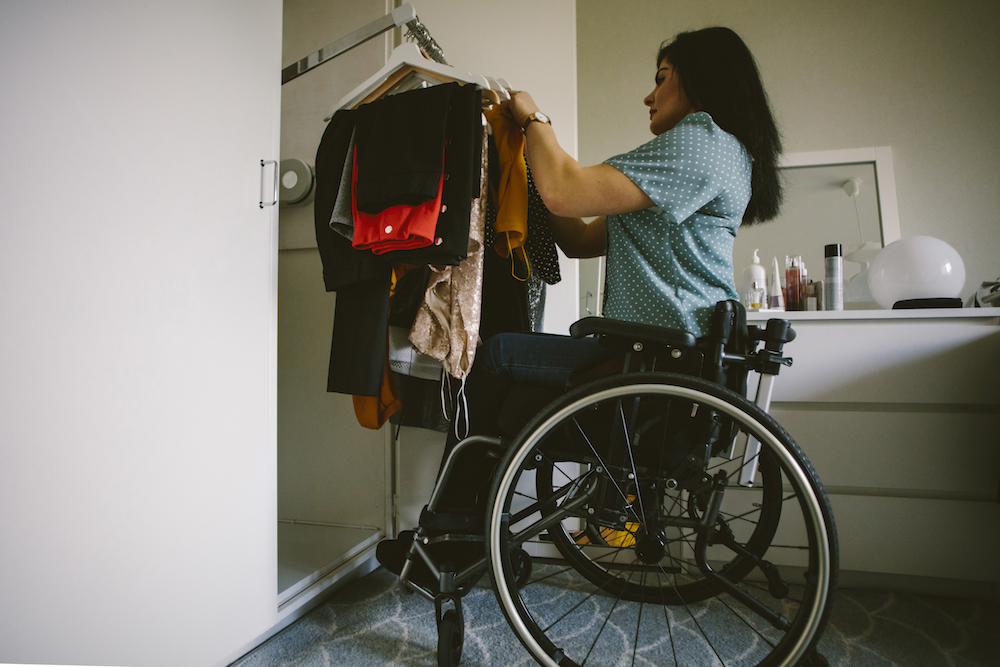 Full length side view of young disabled woman looking at clothes hanging in wardrobe