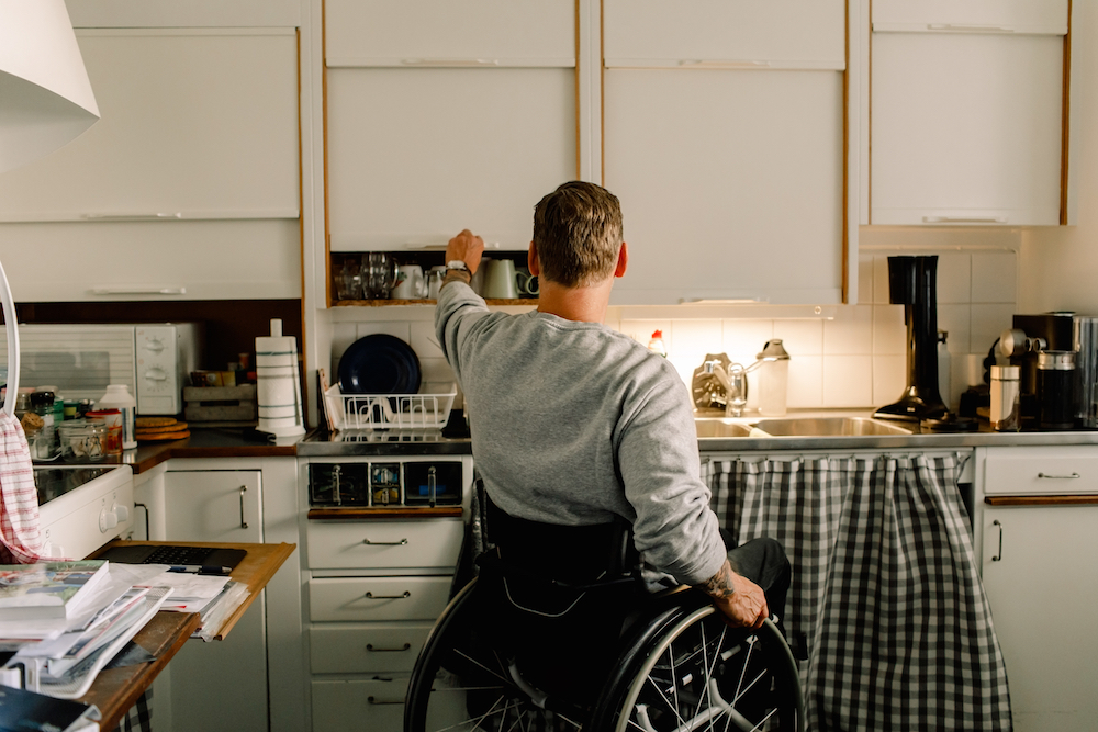 disabled man opening cabinet in white kitchen at home