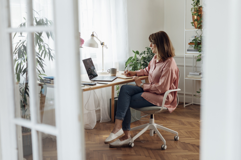 woman sitting at home office desk with window and light