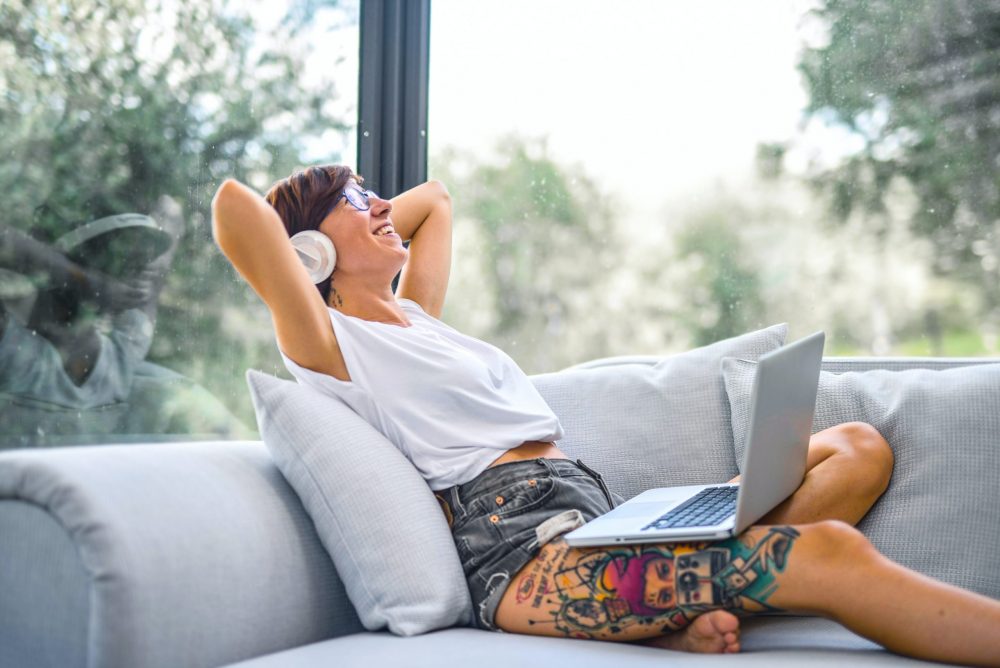 Woman reclining on a couch, headphones over her ears, computer on her lap.