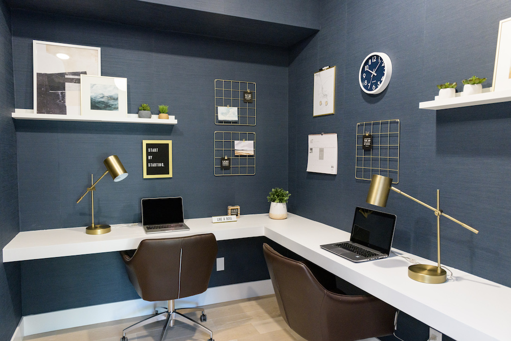 L-shaped white double desk in navy home office with assorted items on hall