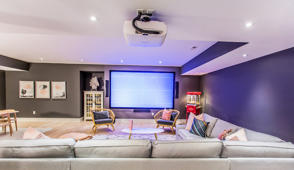 A sleek basement home movie theatre design with oversized TV, speakers and L-shaped couch for plenty of guests