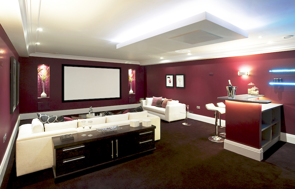 A deep red/maroon basement home theatre with a tiny bar section and plenty of seating