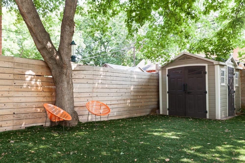 green backyard with shed, fence and two orange chairs